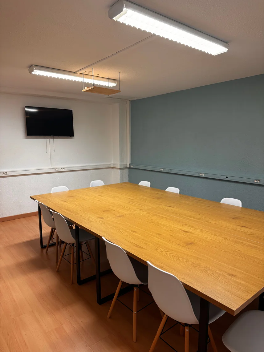 La salle au mur bleu, avec une grande table en bois, des chaises et un écran TV.